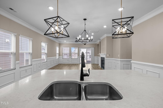 kitchen featuring a sink, decorative light fixtures, light stone countertops, and a glass covered fireplace