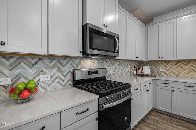 kitchen with light stone counters, backsplash, white cabinetry, light wood-style floors, and appliances with stainless steel finishes