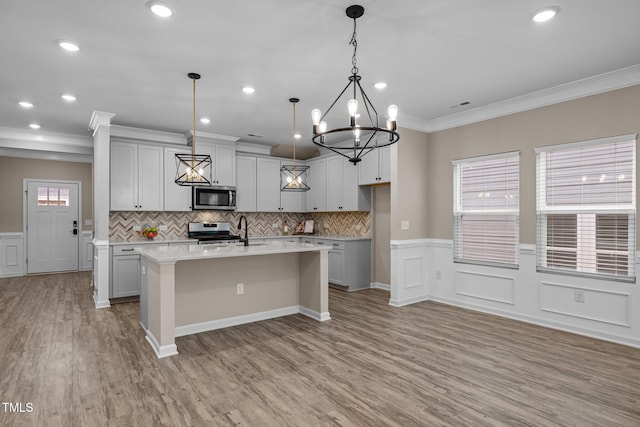 kitchen with an island with sink, a sink, appliances with stainless steel finishes, light wood finished floors, and light countertops