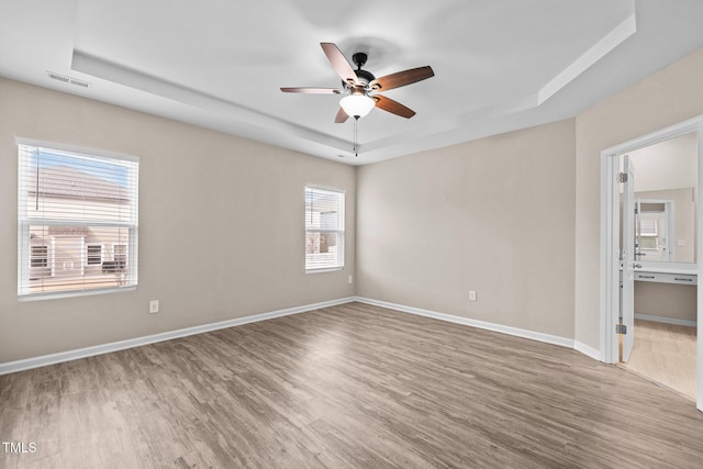 spare room with visible vents, a raised ceiling, baseboards, and wood finished floors