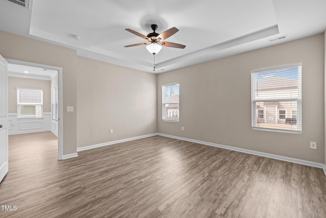 unfurnished room featuring a tray ceiling, wood finished floors, visible vents, and ceiling fan