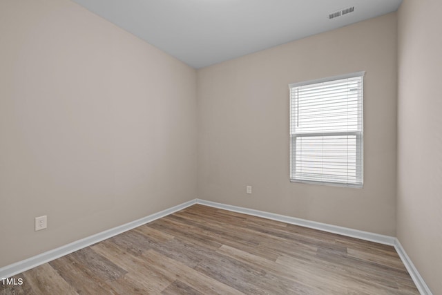 empty room with wood finished floors, visible vents, and baseboards