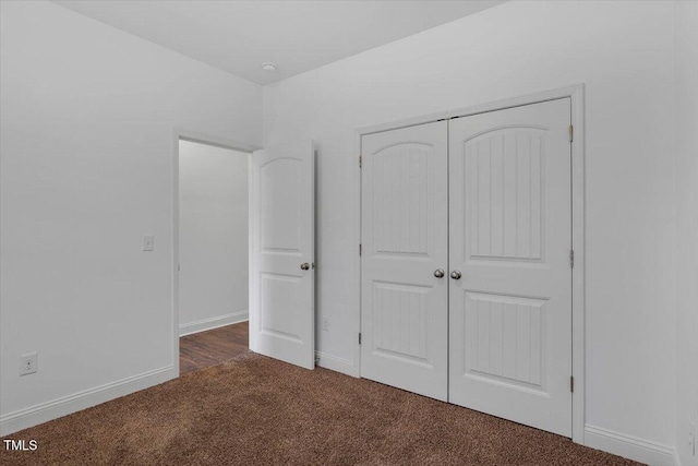 unfurnished bedroom featuring baseboards, a closet, and dark carpet