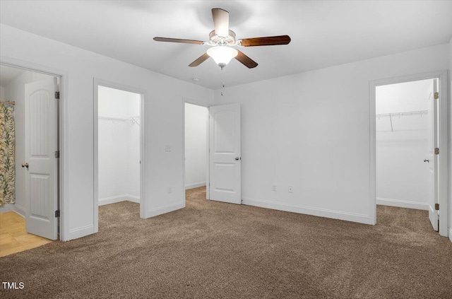 unfurnished bedroom with a spacious closet, baseboards, ceiling fan, light carpet, and a closet