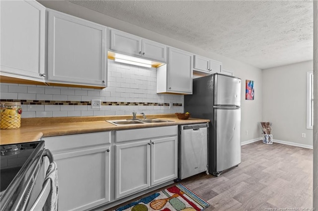 kitchen featuring light wood-type flooring, a sink, tasteful backsplash, stainless steel appliances, and white cabinets