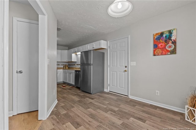 kitchen with visible vents, a textured ceiling, wood finished floors, freestanding refrigerator, and baseboards