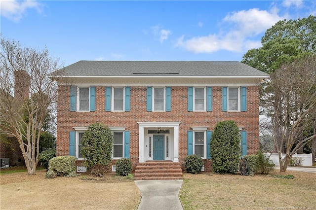 view of front facade with brick siding, a front lawn, and a shingled roof