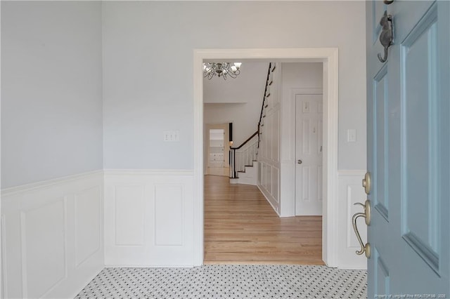 foyer entrance featuring an inviting chandelier, stairway, a decorative wall, and a wainscoted wall