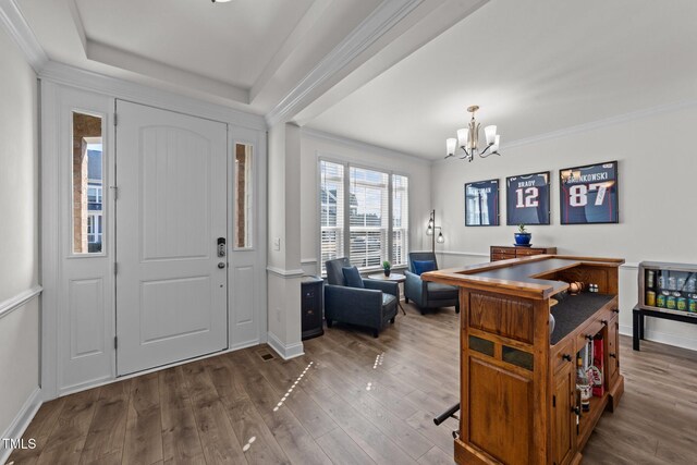 foyer entrance with wood finished floors, baseboards, ornamental molding, a raised ceiling, and a notable chandelier