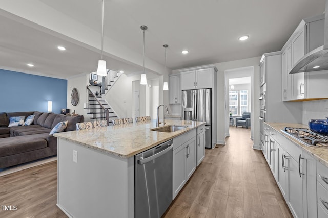 kitchen featuring wall chimney range hood, light wood-type flooring, appliances with stainless steel finishes, and a sink