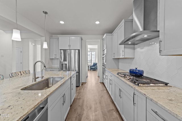 kitchen featuring pendant lighting, a sink, wall chimney range hood, appliances with stainless steel finishes, and light wood finished floors