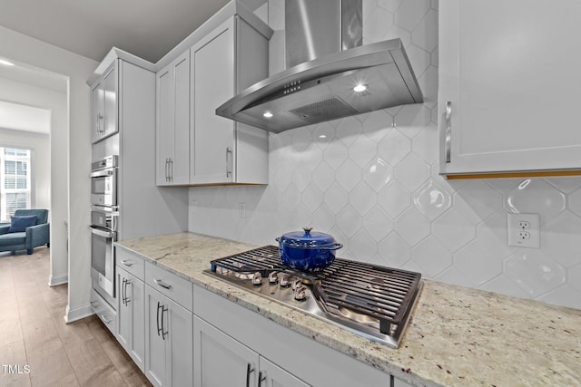 kitchen with light stone countertops, stainless steel gas stovetop, white cabinetry, wall chimney exhaust hood, and tasteful backsplash