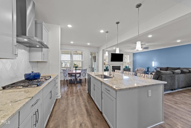 kitchen featuring wall chimney range hood, open floor plan, appliances with stainless steel finishes, and a sink