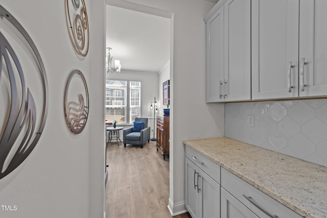 kitchen featuring a notable chandelier, light wood-style flooring, light stone counters, washer / clothes dryer, and decorative backsplash