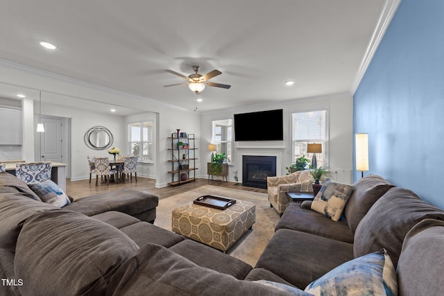 living room with baseboards, ornamental molding, recessed lighting, light wood-style floors, and a glass covered fireplace