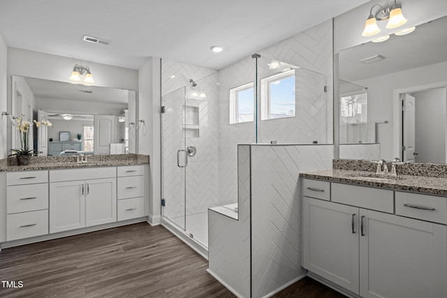 bathroom featuring wood finished floors, visible vents, two vanities, a sink, and a shower stall