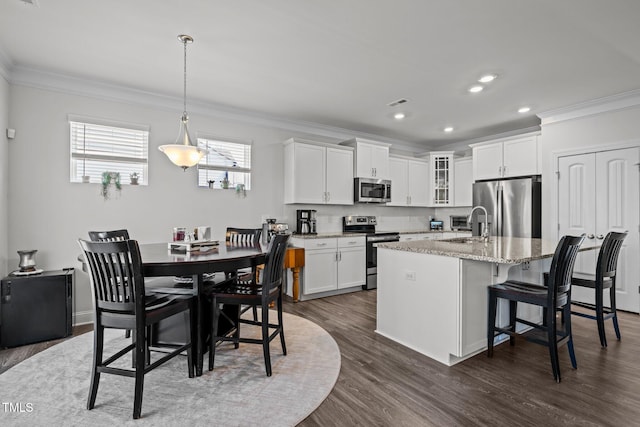 kitchen with light stone counters, dark wood-style flooring, stainless steel appliances, and ornamental molding