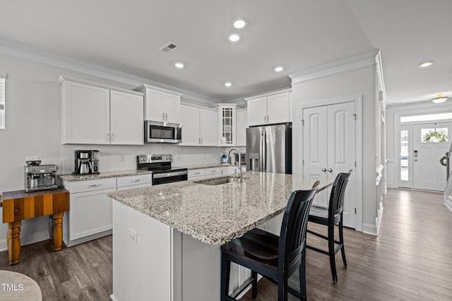 kitchen with a center island with sink, a sink, ornamental molding, dark wood-type flooring, and stainless steel appliances