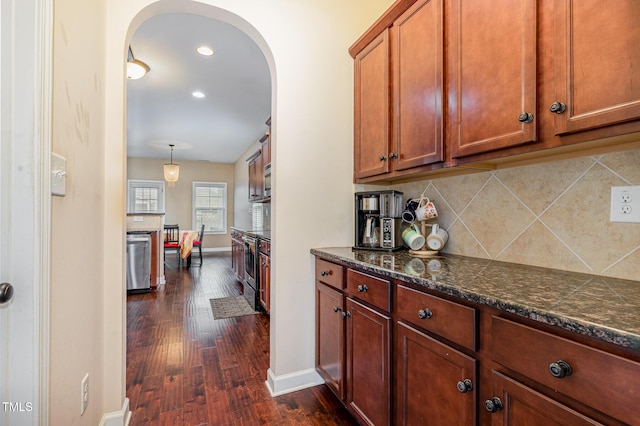 interior space with dark wood-type flooring, arched walkways, appliances with stainless steel finishes, decorative backsplash, and baseboards