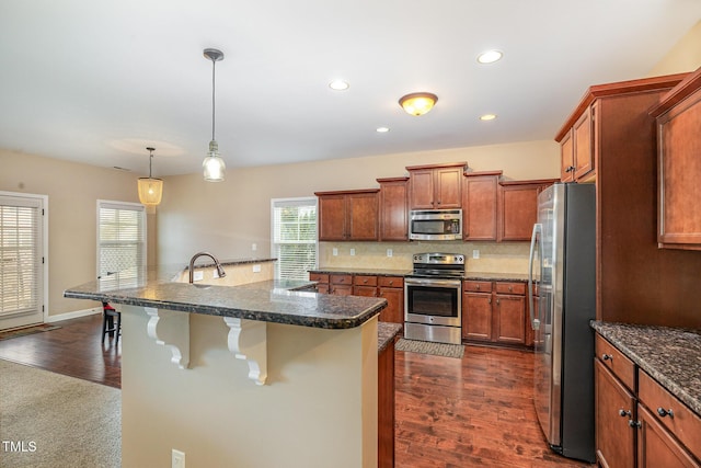 kitchen with backsplash, appliances with stainless steel finishes, a breakfast bar, and dark wood-style flooring