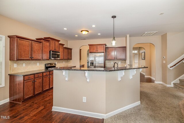 kitchen featuring dark stone countertops, visible vents, arched walkways, stainless steel appliances, and a kitchen breakfast bar