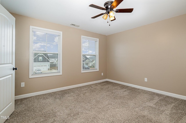 carpeted spare room with visible vents, a ceiling fan, and baseboards