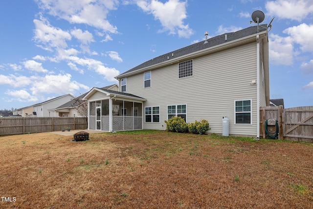 rear view of house featuring a fenced backyard, a fire pit, a lawn, and a sunroom