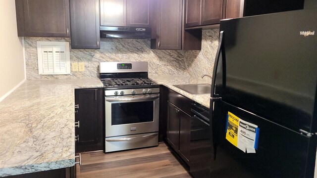 kitchen with dark brown cabinets, under cabinet range hood, freestanding refrigerator, stainless steel gas range, and a sink