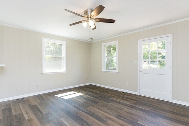 empty room with dark wood finished floors, visible vents, crown molding, and baseboards