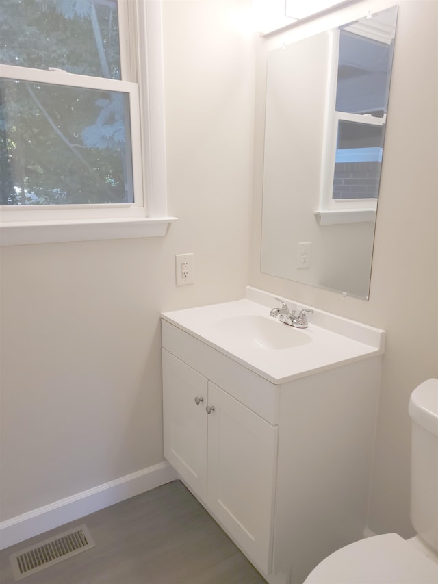 bathroom with visible vents, baseboards, toilet, wood finished floors, and vanity