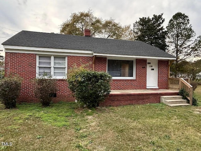 single story home featuring brick siding, a chimney, a shingled roof, and a front lawn