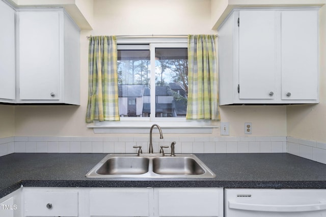 kitchen with dark countertops, dishwashing machine, white cabinetry, and a sink