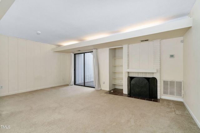 unfurnished living room with carpet flooring, a fireplace, visible vents, and built in shelves