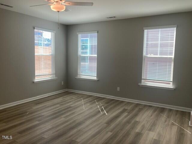 empty room with dark wood finished floors, visible vents, and baseboards