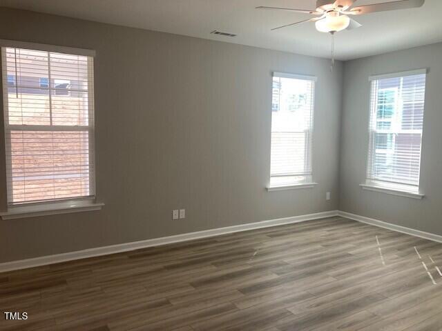 unfurnished room with a wealth of natural light, baseboards, wood finished floors, and ceiling fan