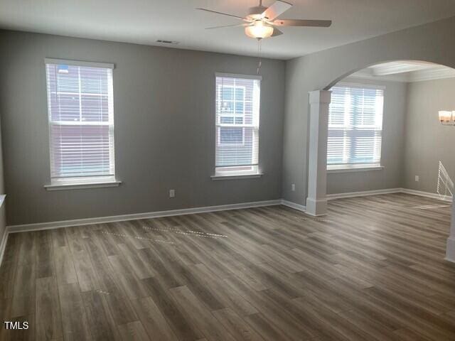 empty room featuring baseboards, arched walkways, dark wood-style floors, and a ceiling fan