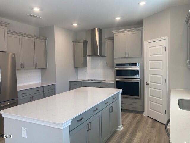 kitchen with stainless steel appliances, a center island, wall chimney exhaust hood, and gray cabinets