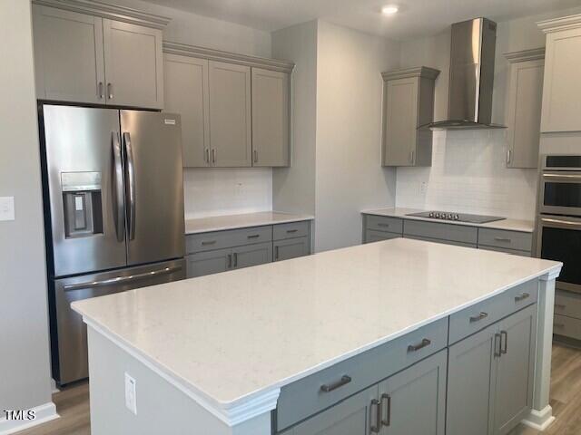 kitchen featuring gray cabinetry, a kitchen island, wood finished floors, stainless steel appliances, and wall chimney range hood