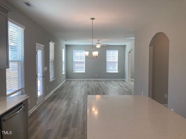 unfurnished dining area featuring wood finished floors, baseboards, visible vents, arched walkways, and a notable chandelier