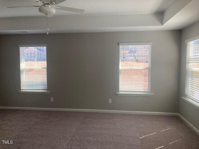 empty room featuring a tray ceiling, baseboards, carpet floors, and a ceiling fan