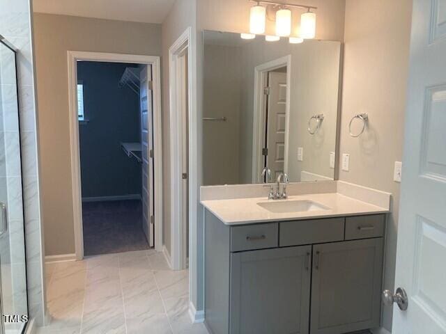 full bathroom with a walk in closet, baseboards, a tile shower, marble finish floor, and vanity