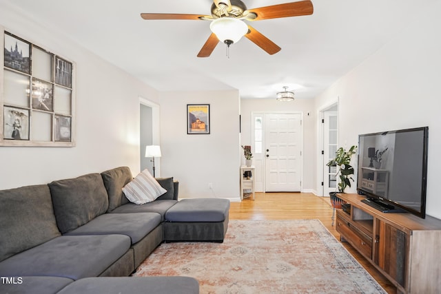 living room featuring a ceiling fan, baseboards, and light wood finished floors