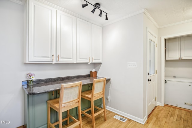 office featuring baseboards, visible vents, light wood-style flooring, track lighting, and crown molding