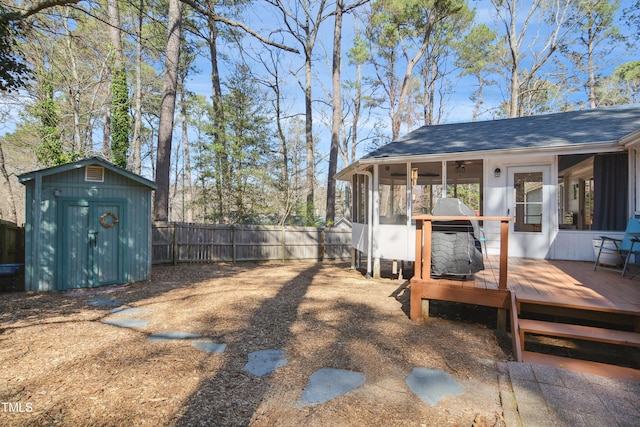 view of yard featuring an outbuilding, a shed, a wooden deck, a fenced backyard, and a sunroom