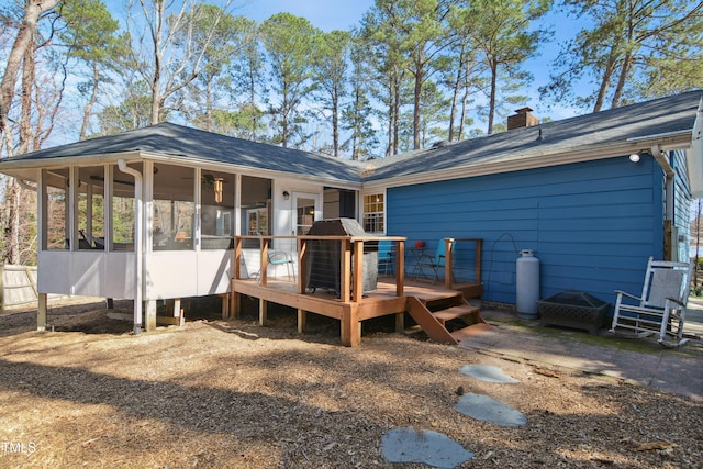 rear view of property with a chimney, a deck, and a sunroom