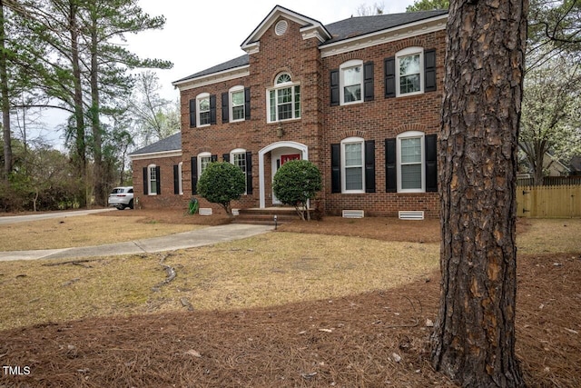 view of front of property with brick siding, roof with shingles, a front lawn, and fence