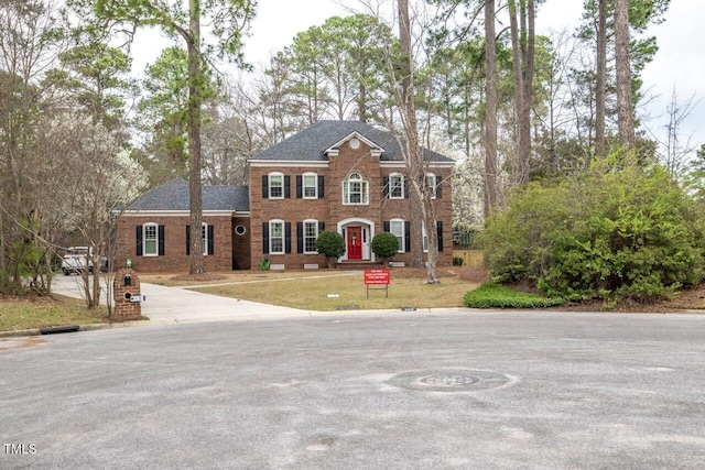 view of front of property featuring brick siding, roof with shingles, and a front lawn