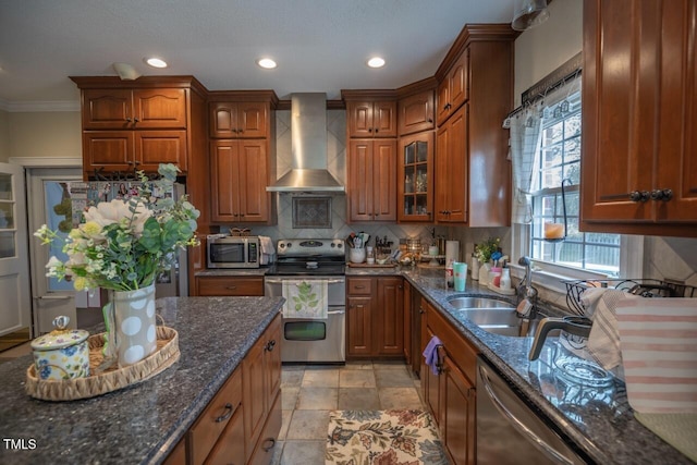 kitchen with brown cabinets, a sink, backsplash, stainless steel appliances, and wall chimney exhaust hood