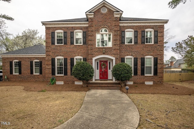 view of front facade with brick siding, a front lawn, roof with shingles, and fence