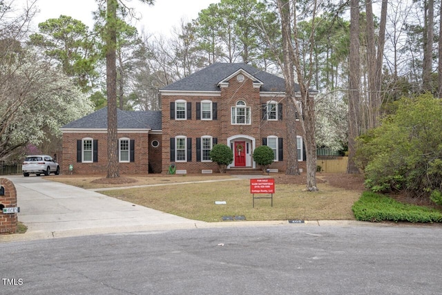 view of front of home with brick siding, concrete driveway, a front yard, and a shingled roof